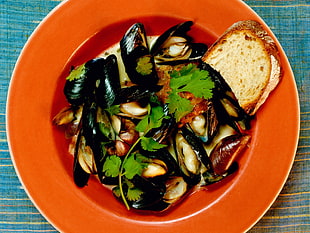 saute mussel shells with sliced of bread on orange soup bowl