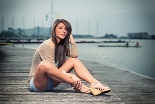 woman sitting on gray wooden sea dock