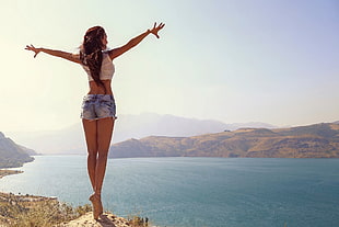 woman in white crop top and micro denim shorts standing on the hill during daytime