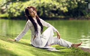 woman sitting on green grass near body of water
