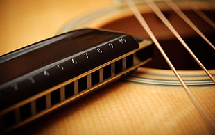 selective focus photography of black harmonica on top of brown guitar