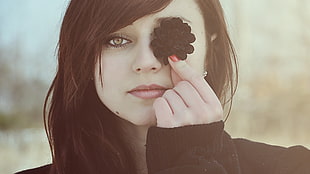 woman wearing black sweater covers her eye with a black flower