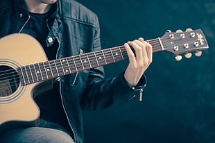man in black jacket playing brown cut away guitar