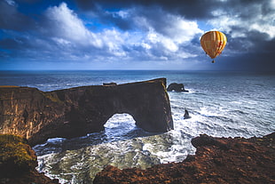hot air balloon floating above sea near boulders