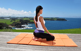 woman wearing white tank top sitting on mat in front of sea