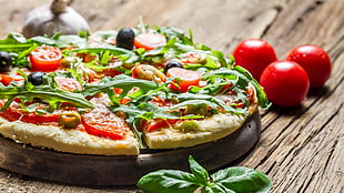 Pizza on brown wooden tray near three red tomatoes