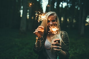 depth of field photography blonde haired woman wearing black cardigan holding lighted incenses