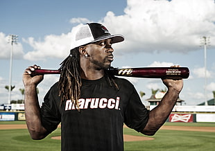 man wearing black Marucci shirt holding red baseball bat