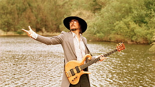 man in grey blazer with electric guitar standing beside body of water during daytime