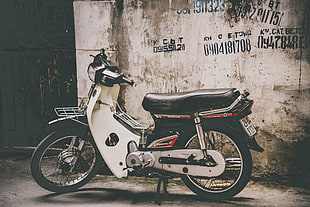 white and black underbone motorcycle in front of wall