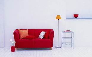 photo of empty red 2-seat sofa with throw pillows, orange lampshade floor lamp, and gray metal 2-layered shelf