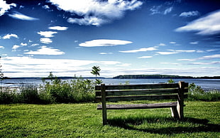 gray wooden bench on green grass field under cloudy blue sky
