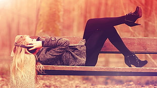 woman lying on brown bench holding headphones