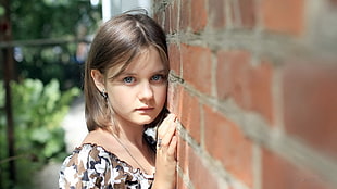 shallow focus photography of girl wearing brown and white floral top beside of brick wall