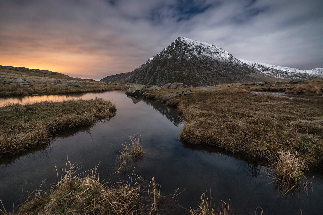 landscape photo of river between grass under snow covered mountain, snowdonia
