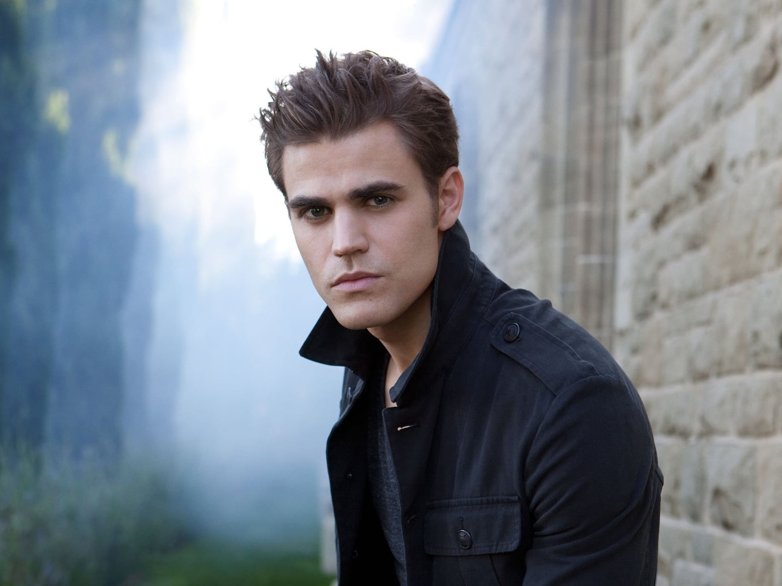 portrait photo of male wearing black jacket beside gray concrete wall