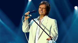 man wearing white blazer with white inner shirt holding black microphone on stand