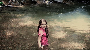 girl wearing pink shirt standing on body of water during daytime