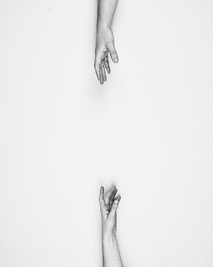 two hands reaching each other in gray scale photo