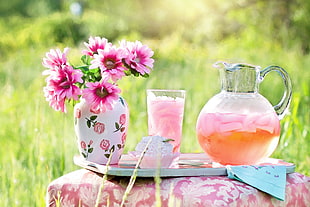 pink petaled flower in white and pink floral vase beside glass pitcher and drinking glass on tray