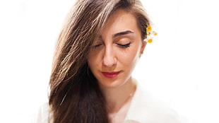 woman in white top, yellow flower on ear with closed eye