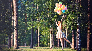 woman standing reaching for balloons near trees during daytime