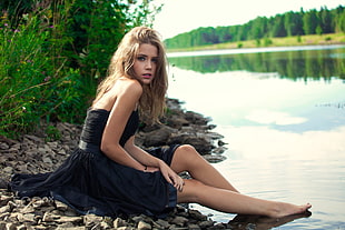 woman in black dress sitting beside body of water