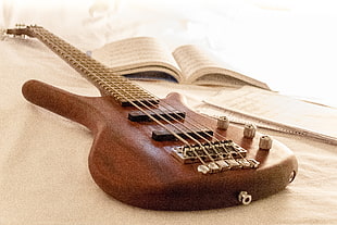 brown electric guitar near opened book on white mattress