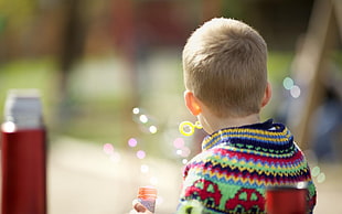 boy in multicolored sweater playing bubble in selective focus photography