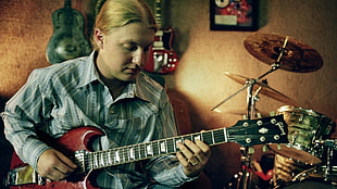 man in gray flannel shirt playing red electric guitar