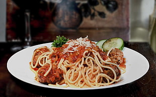 spaghetti with sauce and meatballs on top of round white plate