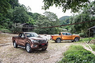two brown and orange crew-cab pickup trucks parked beside river near brown hanging bridge