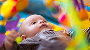 selective focus photography of baby in black shirt lying on activity mat