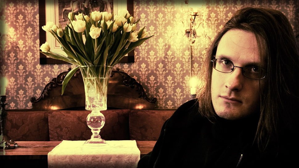 photo of man in black shirt sitting beside white petaled flower on table centerpiece HD wallpaper