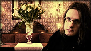 photo of man in black shirt sitting beside white petaled flower on table centerpiece