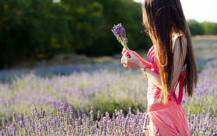 selective photo of woman in pink sleeveless shirt and pink bottoms holding purple petaled flowers