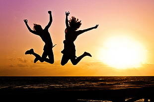 two women jumping near seashore against sunset HD wallpaper