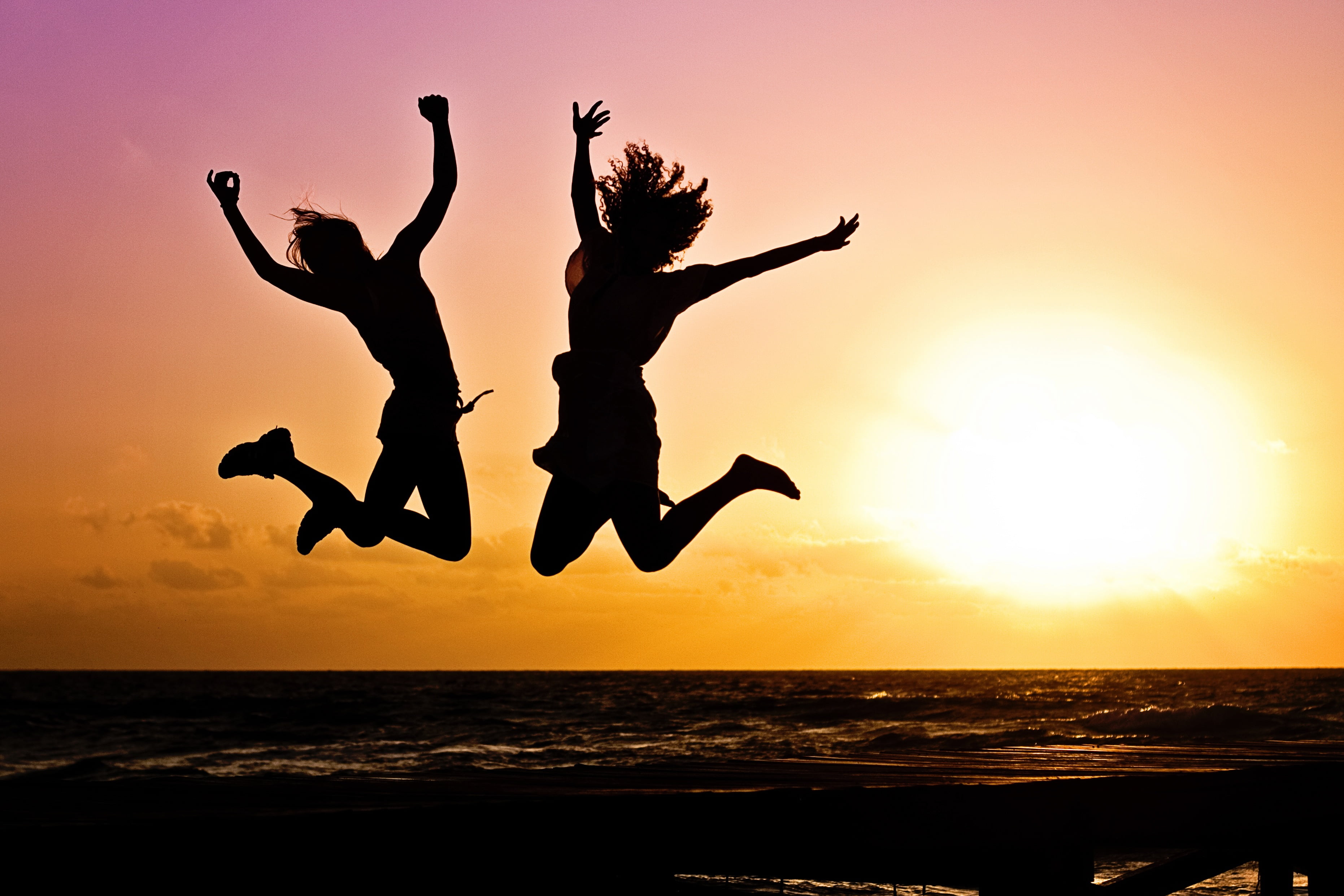 two women jumping near seashore against sunset