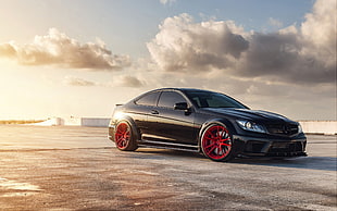 black sports coupe with red wheels under white clouds