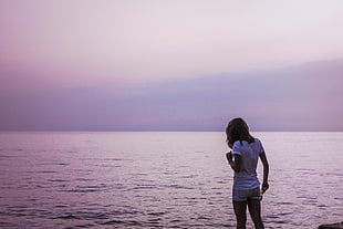 woman in white t-shirt and blue shorts standing beside beach