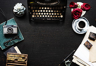black and white typewriter beside artificial red roses on black wooden table