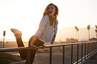 woman wearing white denim jacket holding metal rails smiling during golden hour