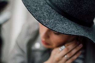 woman wearing grey and black hat holding her earrings