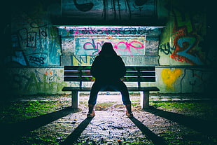 person sitting on bench behind graffiti wall