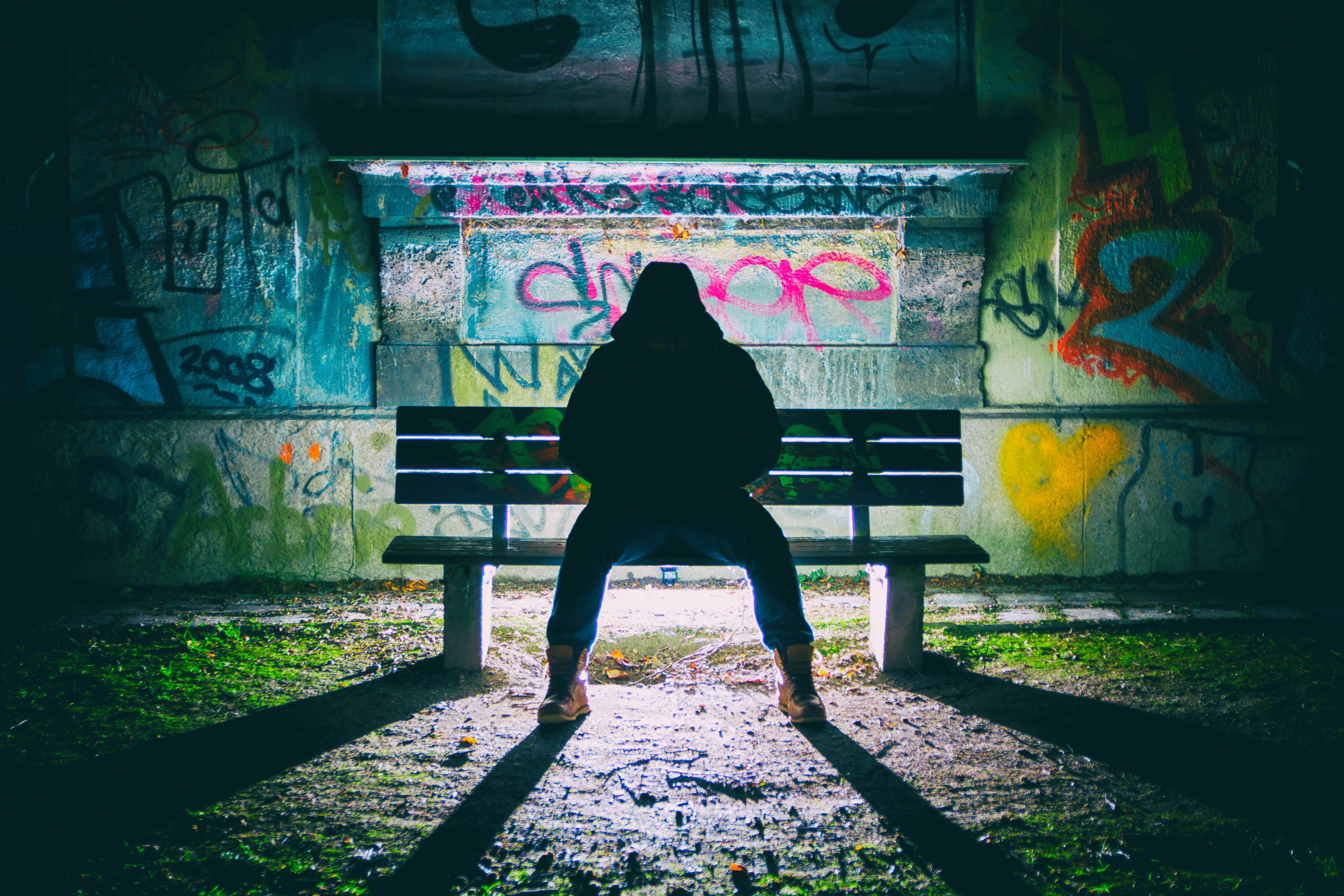 person sitting on bench behind graffiti wall