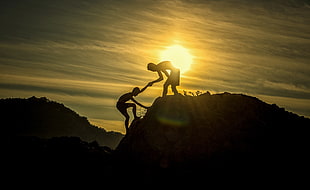 silhouette photo of two men on top of cliff