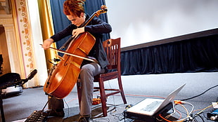 man playing cello on brown wooden chair