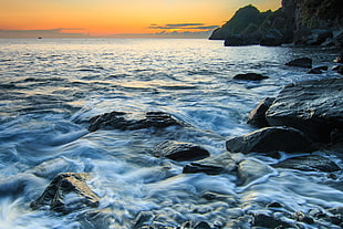 timelaps photo of ocean waves on rocks during sunset