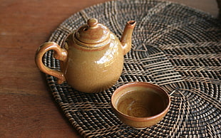 brown ceramic teapot beside bowl on black wicker mat