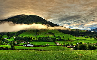 green grass field near village houses and mountains under white cloudy sky during daytime HD wallpaper